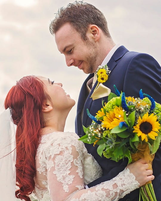 Bride with sunflower wedding bouquet looking into groom's eyes - Picture by Rebecca Gurden Photography