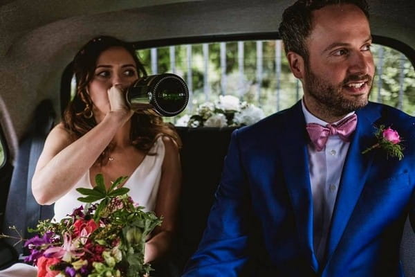 Bride drinking straight from champagne bottle in back of wedding car with groom - Picture by York Place Studios