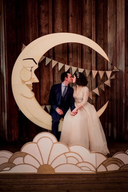 Bride and groom kissing whilst sitting on a crescent moon with a face - Picture by Nordica Photography