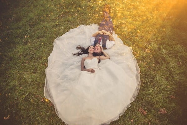 Bride and groom laying on bride's dress on grass - Picture by Him and Her Wedding Photography