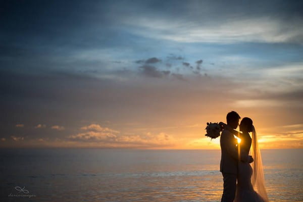 Silhouette of bride and groom in front of the sea with sun shining between them - Picture by darinimages