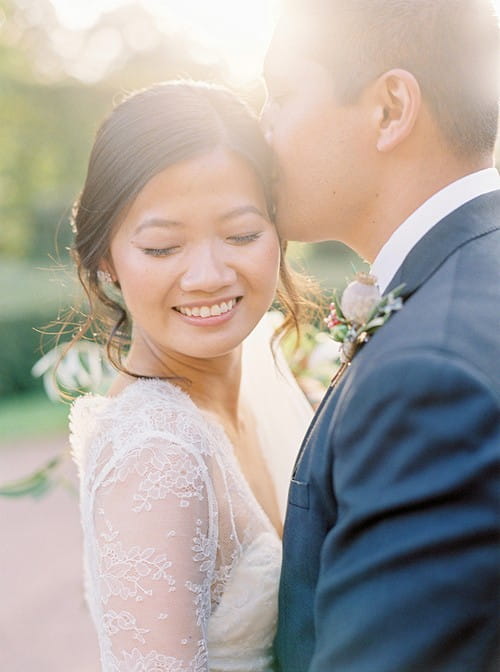 Bride smiling with eyes shut as groom kisses her on the head - Picture by 2 Brides Photography