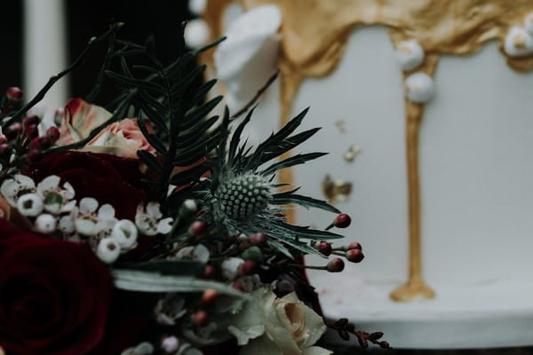 Bouquet with roses and thistles in front of wedding cake