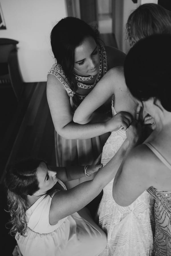 Bridesmaids helping bride get into wedding dress