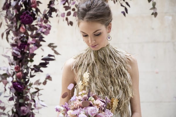 Bride with feather collar bridal neckpiece looking down at purple bouquet