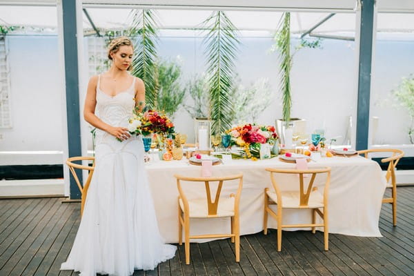 Bride with colourful bouquet standing next to wedding table with tropical styling