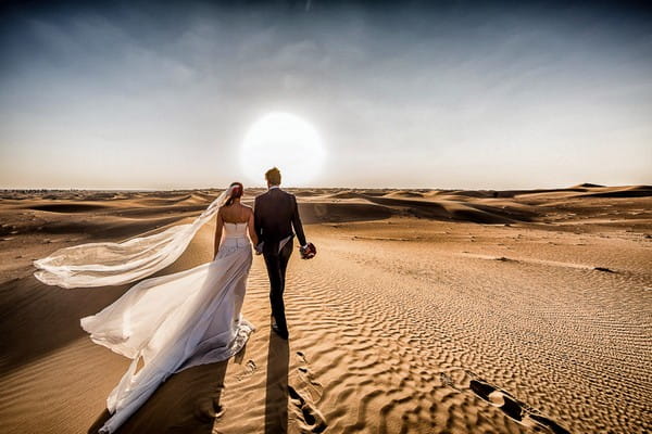 Bride and groom walking across desert towards the sun - Picture by Cristiano Ostinelli Studio