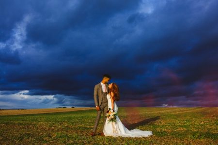 Bride and groom looking at each other with dark blue clouds behind them - Picture by Clare Tam-Im Photography