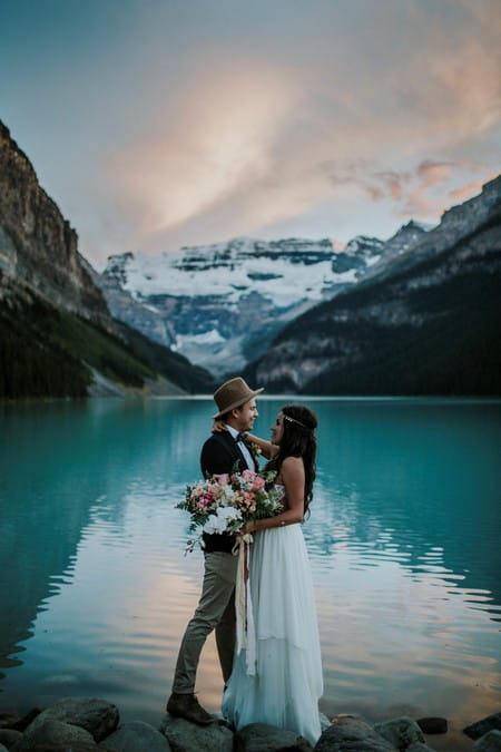 Bride and groom in front of a lake with snow covered mountains in background - Picture by Dawn Photography