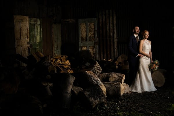Bride and groom standing by logs and old doors - Picture by Sky Photography