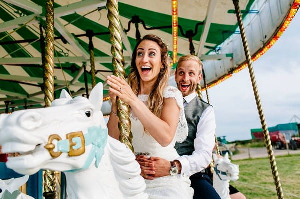 Bride and groom with big smiles as they ride fairground carousel - Picture by Epic Love Story
