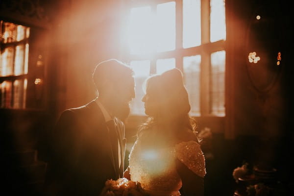 Bride and groom in front of a window as sun shines through - Picture by Joanna Nicole Photography