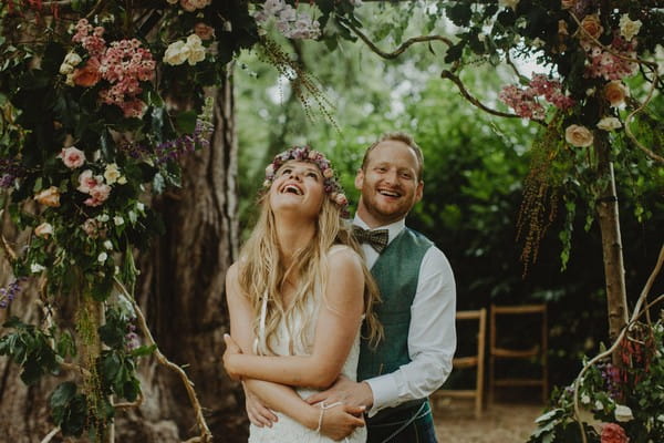 Groom and bride with flower crown laughing under floral arch - Picture by The Curries