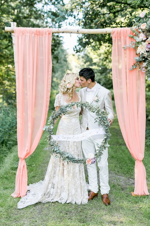 Bride and groom kissing holding large wreath