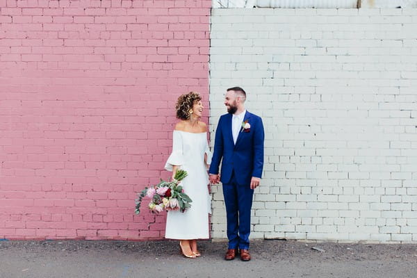Bride and groom standing against pink and white wall