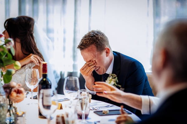 Groom with hand over his eyes as he listens to best man speech