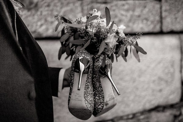 Groom carrying bride's shoes and bouquet