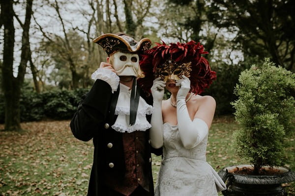 Bride and groom in Georgian outfits wearing Venetian masks