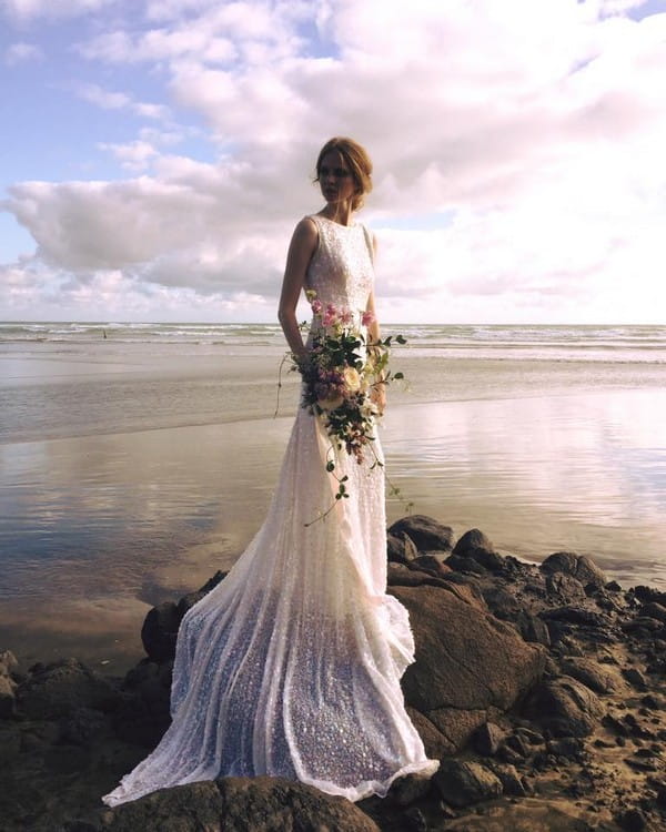 Bride standing on rocks in front of sea - Picture by Katie Grant Photography