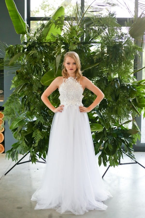 Bride with hands on hips in front of palm leaf backdrop