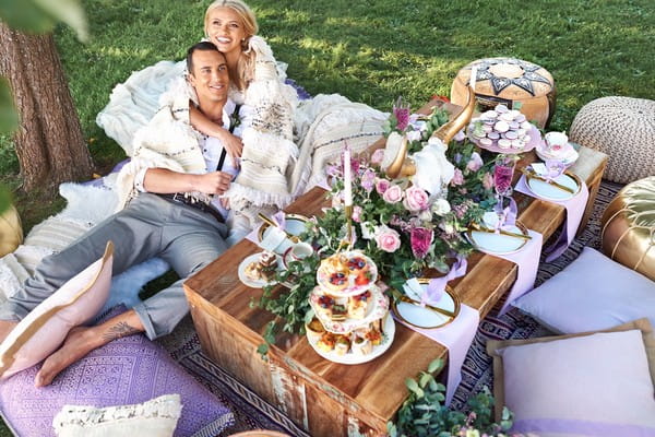 Bride and groom laying on cushions by outdoor wedding table