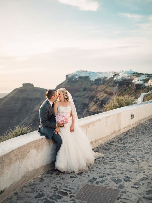 Bride and groom sitting on wall in Santorini