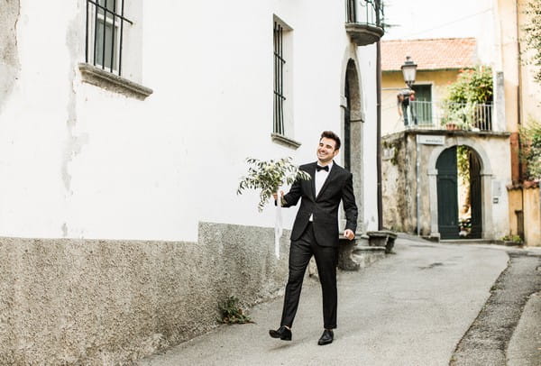 Groom carrying bride's bouquet down street in Lake Como