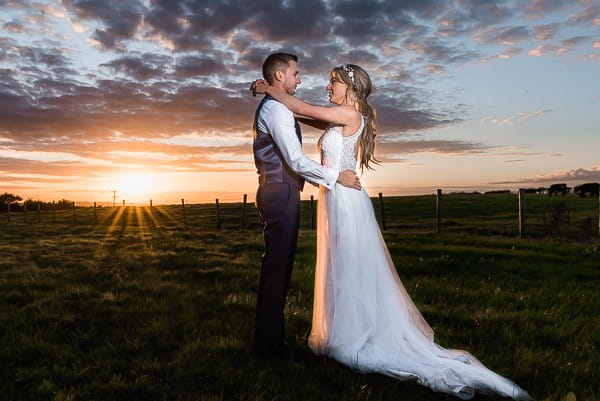 Bride and groom in field as sun sets