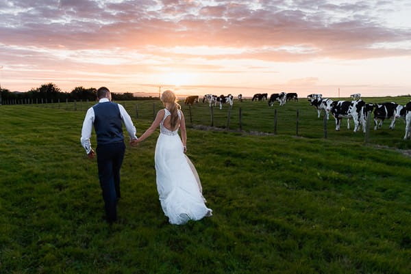 Bride and groom walking across field at farm