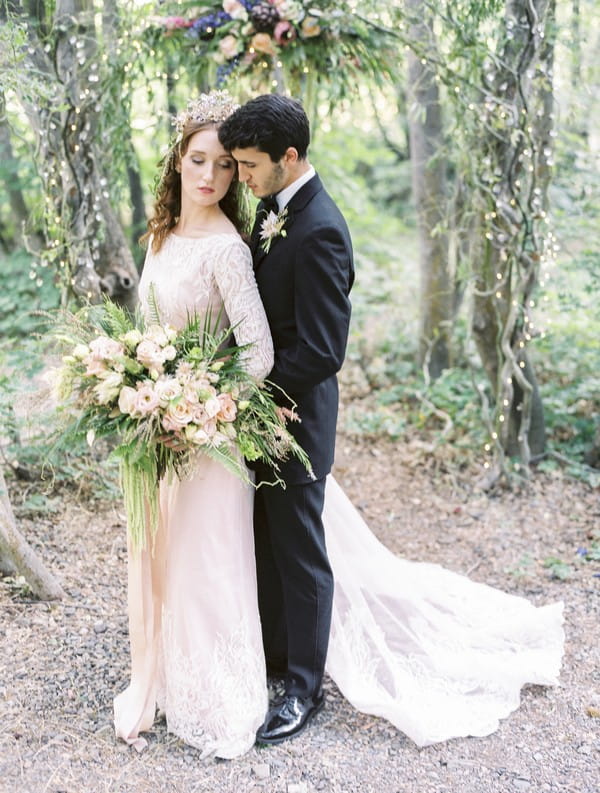 Groom standing behind bride in woods