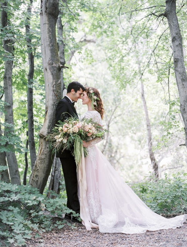 Bride and groom touching heads in woods