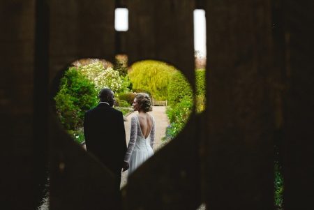 Bride and groom seen through heart shaped hole in gate - Picture by Anesta Broad Photography
