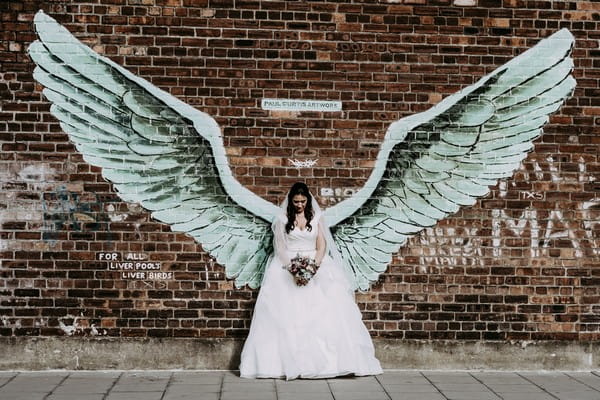 Bride standing against wall with huge wings on it - Picture by Ian MacMichael Photography