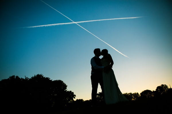 Bride and groom kissing with a vapour trail cross above their heads - Picture by Ketch 22 Photography