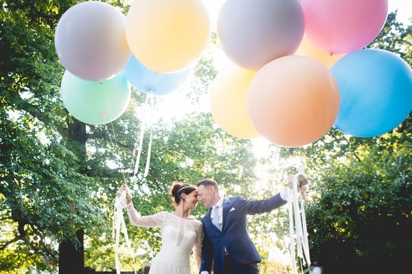 Bride and groom touching heads holding colourful balloons - Picture by Nicola Norton Photography