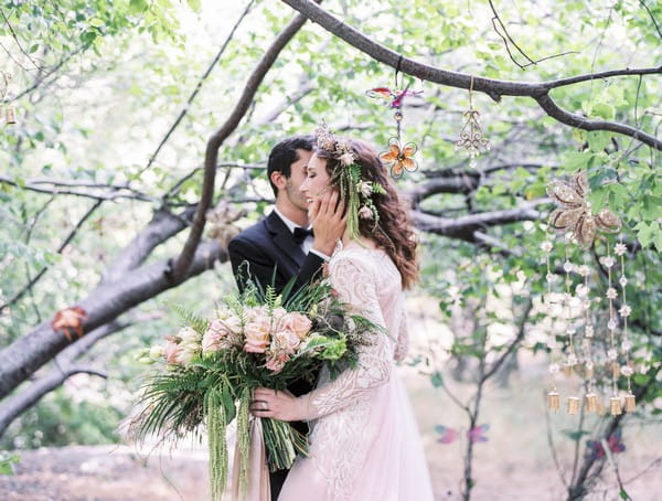 Groom kissing bride on the cheek under tree branches