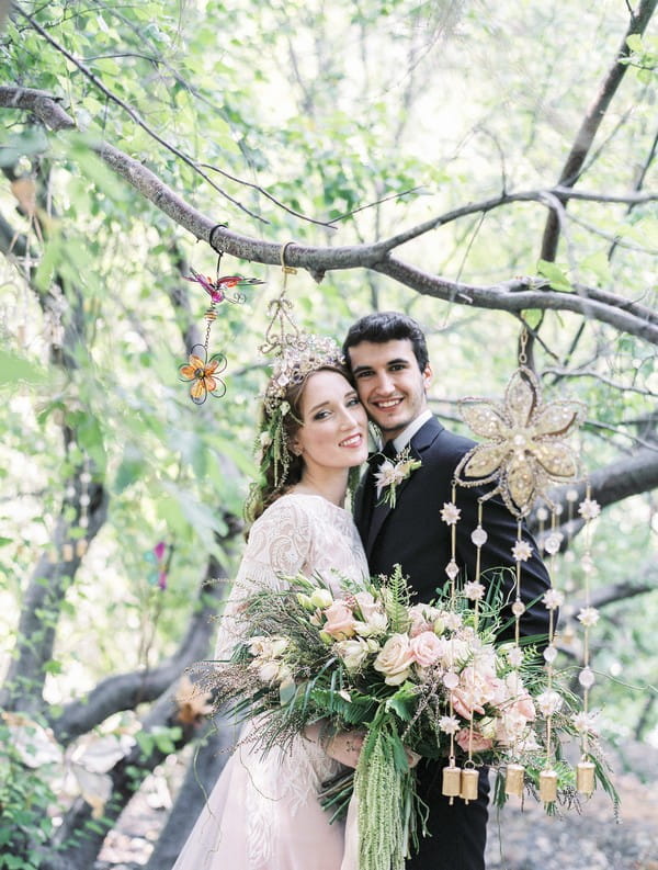 Bride and groom standing under tree branches in woods