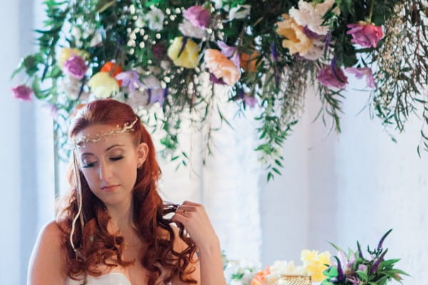 Bride sitting under hanging floral arrangement