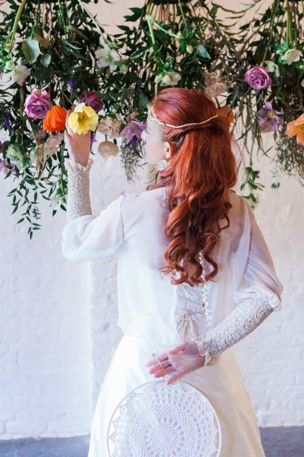 Bride looking at flower holding dreamcatcher behind her back