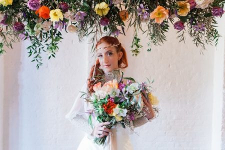 Bride holding colourful bouquet under hanging floral arrangement