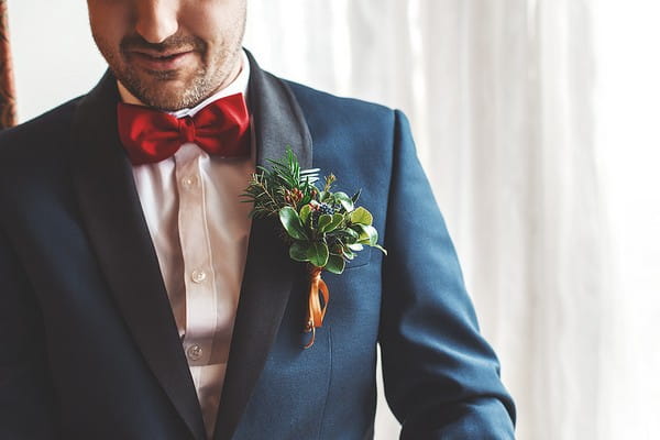 Groom wearing red bow tie, blue jacket and Christmas buttonhole