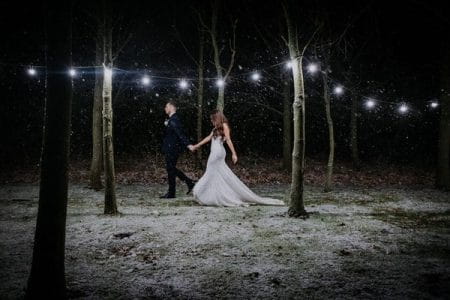 Bride and groom walking through trees in snow at night - Picture by Shoot It Momma