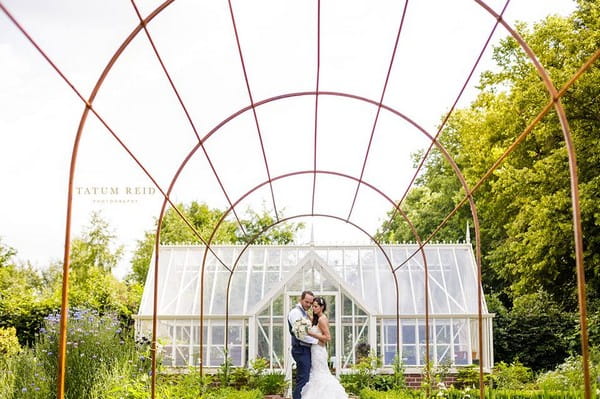 Bride and groom standing in front of large greenhouse - Picture by Tatum Reid Photography