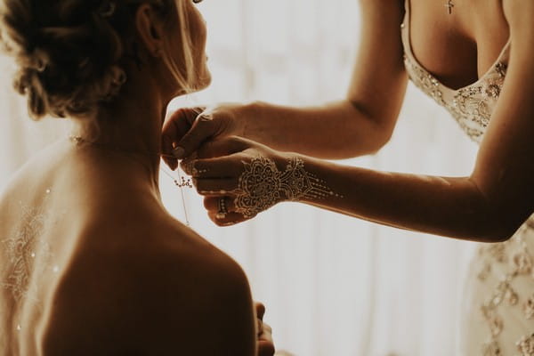 Woman with henna hand drawing helping bride put on necklace - Picture by India Earl Photography