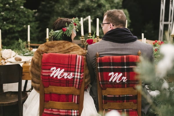 Bride and groom sitting on wedding chairs with Mr and Mrs blankets