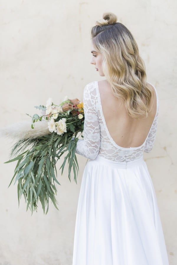 Bride wearing open back wedding dress holding large trailing bouquet