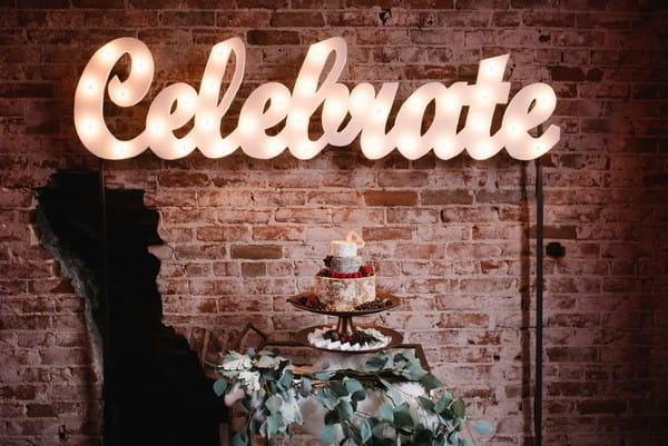 Neon celebrate sign above cheese stack wedding cake