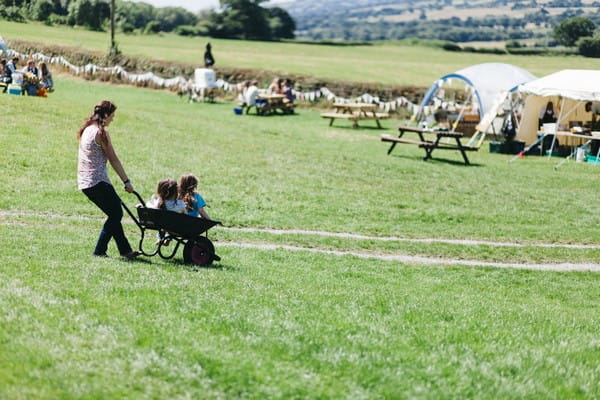Woman pushing children in wheelbarrow across field at festival wedding
