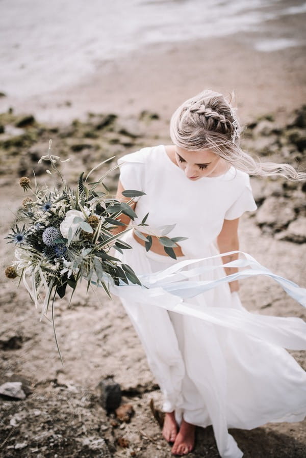 Bride carrying bouquet on beach