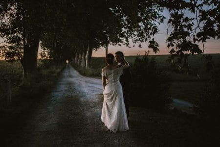 Bride and groom standing on track lined with tress - Picture by Green Antlers Photography